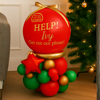 Classic Red & Green Elf Pop Me Balloon with festive decorations by a Christmas tree.