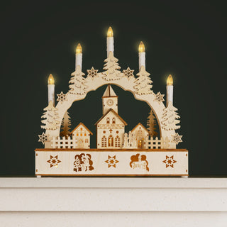 Christmas Village Candle Bridge with glowing LED lights and miniature snow-topped houses on a cozy mantel.