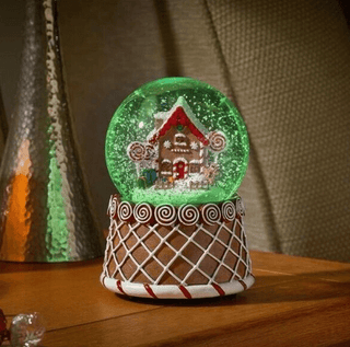 Christmas Gingerbread Snow Globe Musical LED Light with gingerbread scene and color-changing LEDs on a wooden table.
