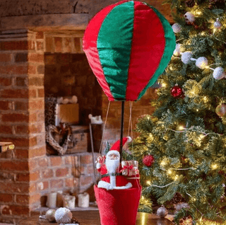 Festive Christmas Hanging Santa Decoration in a hot air balloon, featuring Santa Claus in a red suit, next to a decorated Christmas tree.