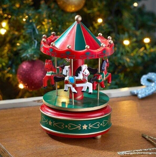 Christmas Carousel Musical Decoration on festive table setting, featuring rotating horses with Christmas tree in background.