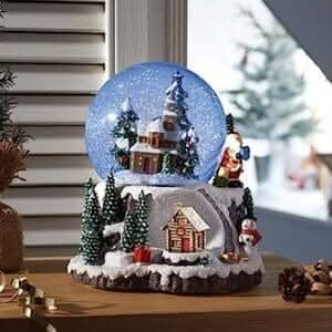 Christmas Village Winter Wonderland color changing musical snow globe with snow-dusted cottages and evergreen trees on a wooden table.